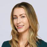 A woman with long, blonde hair and light eyes smiles slightly. She is wearing a teal top and is posed against a plain, light gray background.