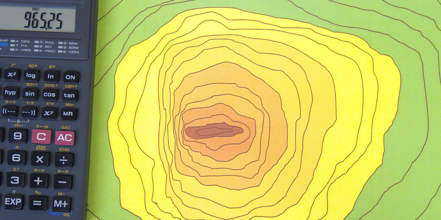 A scientific calculator sits next to a colorful topographic map with contour lines forming concentric shapes in shades of yellow, green, and brown.