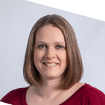 A woman with straight, shoulder-length light brown hair and fair skin smiles at the camera. She is wearing a maroon top and is posed in front of a plain light background.
