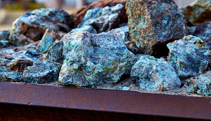 A close-up view of several rough, blue-green mineral rocks piled together in a rusty metal container.