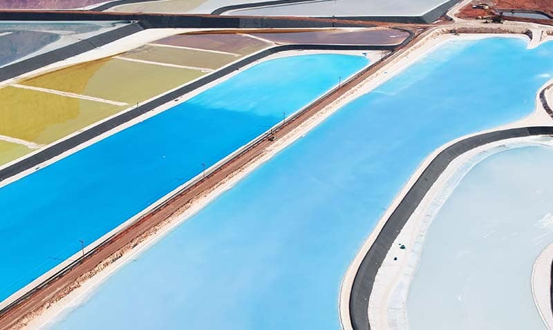 Aerial view of large, geometric salt evaporation ponds with sections of vivid blue and pale colors separated by earthen barriers.