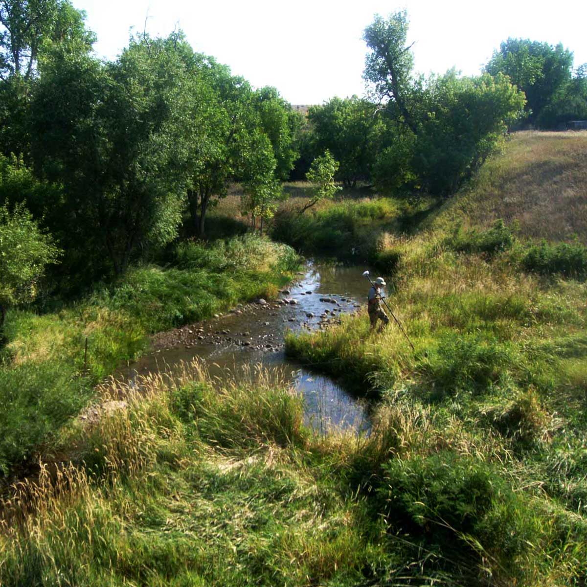 A surveyor alongside a stream running through green hills